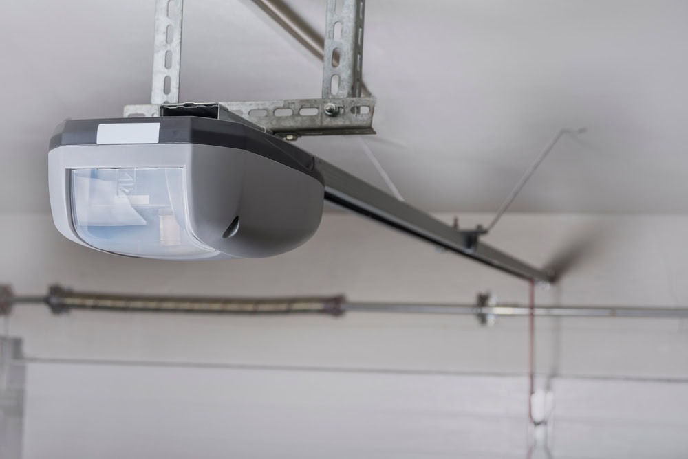 Close-up view of a modern garage door opener attached to the ceiling, showing its motor housing, metal rail, and support brackets in a residential garage.