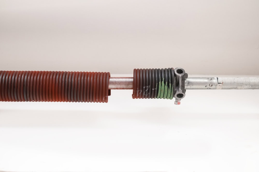 A close-up of a metal rod with a red and black corrugated, cylindrical covering, possibly part of a spring or mechanical component, set against a plain white background.